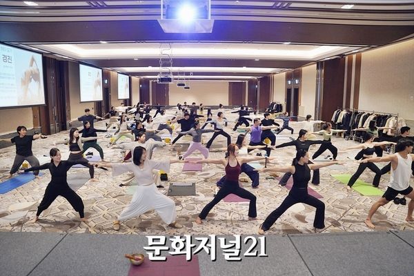 기부요가페스티벌 — 대형 홀에서 참가자들이 함께 전사 자세를 취하는 모습